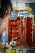 Large glass vessel labeled as Midsummer Mint filled with amber colored brewed tea